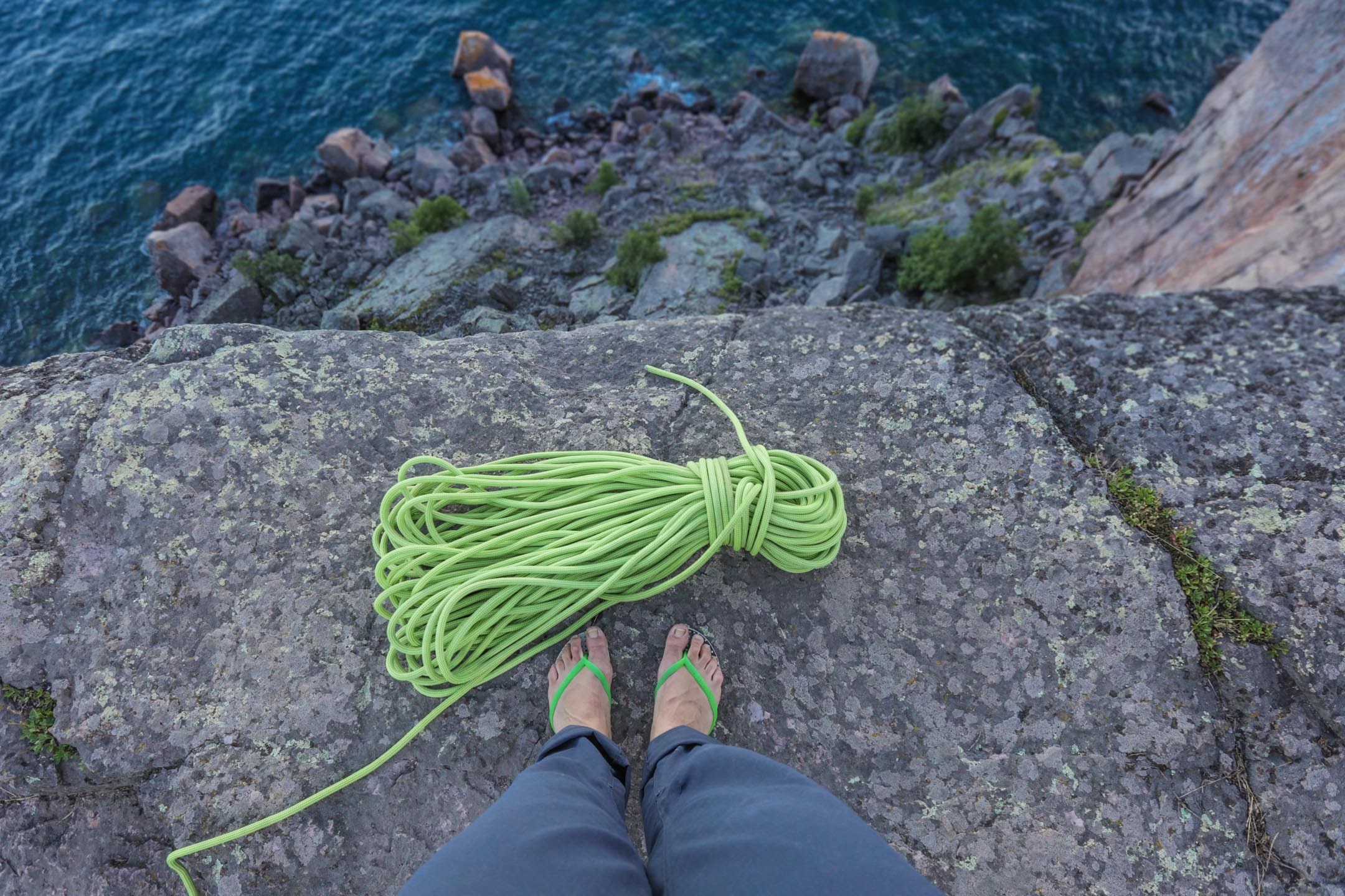 A coiled rope and flip-flops on rock above the water