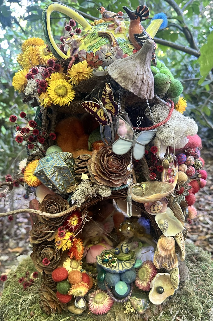 An elaborate fairy house built from dried flowers, pinecones, shells, a butterfly, and tiny treasures