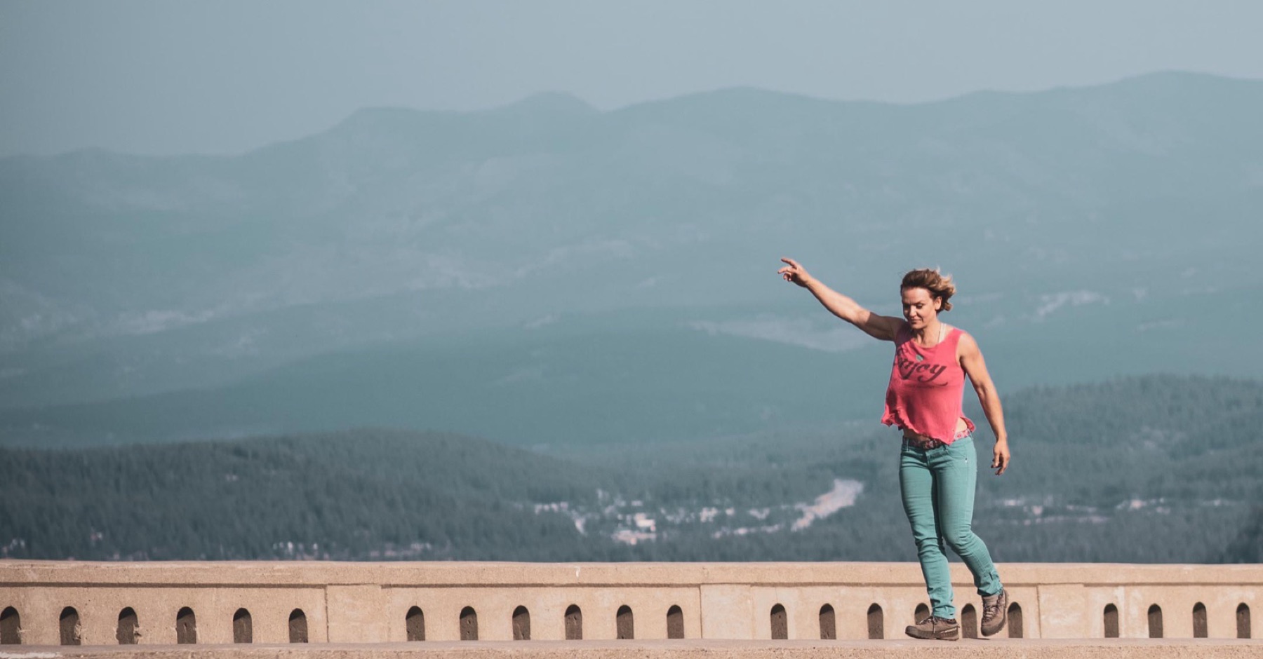 Marta walking a stone parapet, arm out for balance, mountains beyond