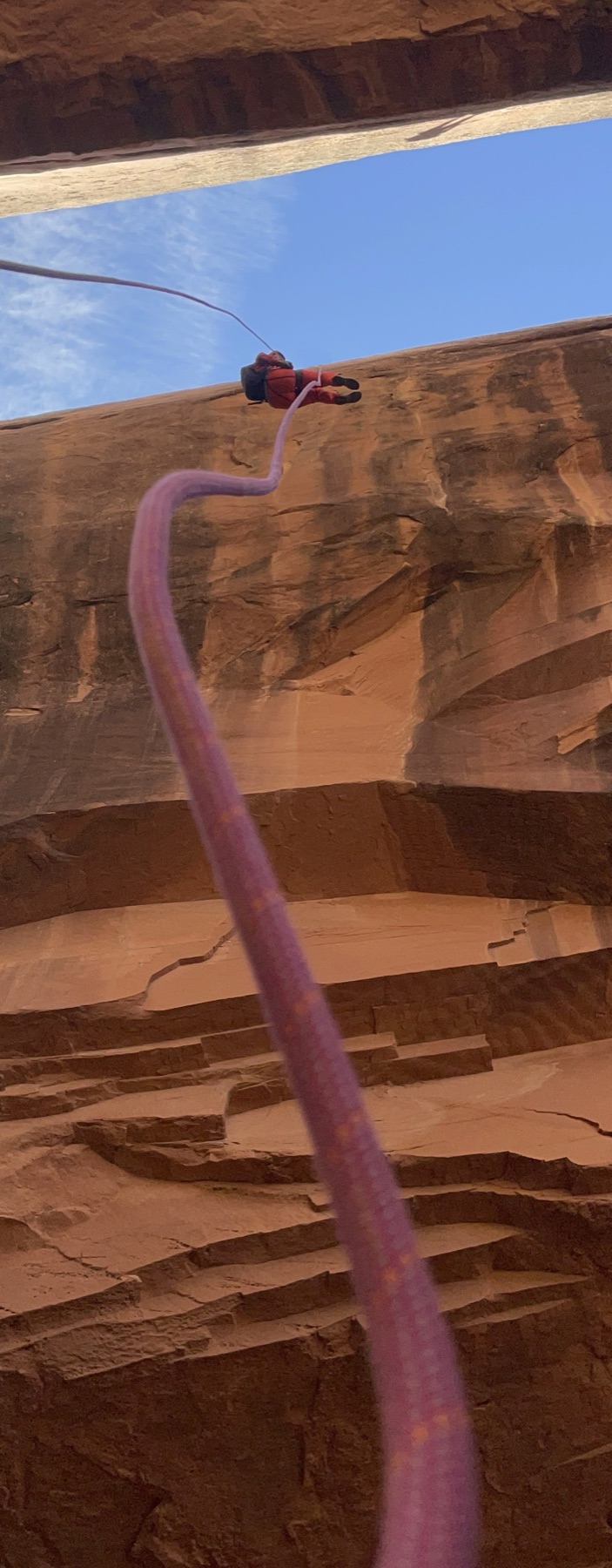 A rope dropping the full height of a red sandstone wall to a climber at the top
