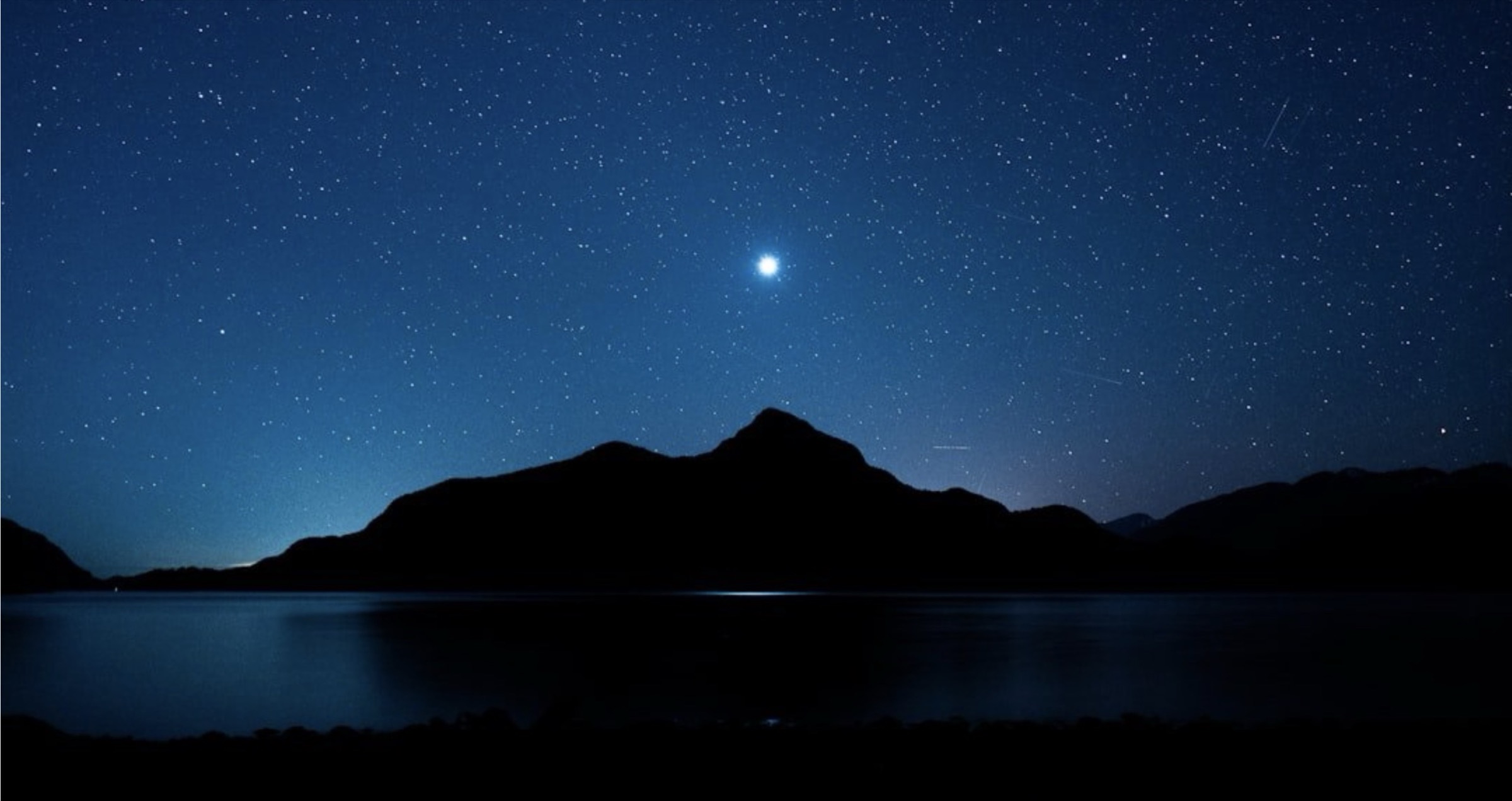 A star-filled night sky over a dark mountain and still water
